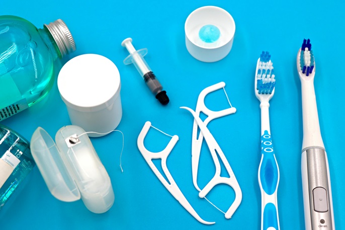 Different dental floss types, toothbrushes, bottles, and a syringe on a blue table. 