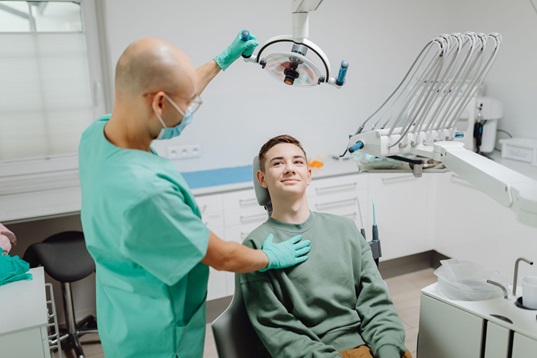 Dental technician wearing scrubs adjusts X-ray tools for patient